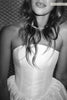 Black and white close-up of a woman wearing a strapless corset-style dress with a ruffled skirt and a delicate necklace.