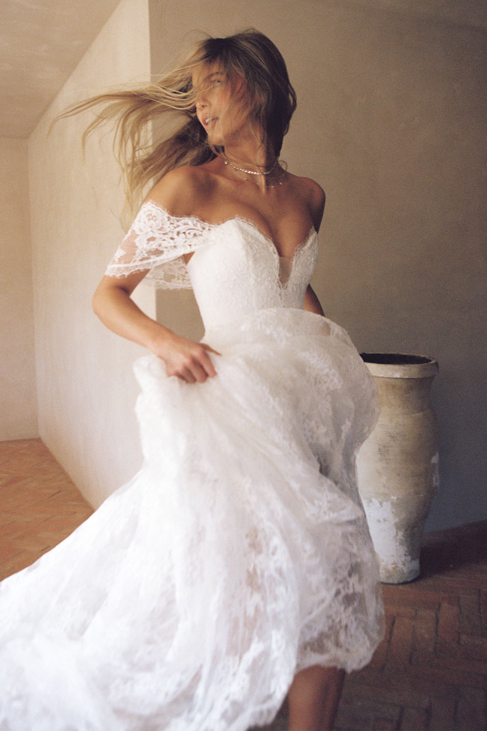 A woman wearing a white off-the-shoulder lace wedding gown with a deep V neckline and a full layered skirt_XS_