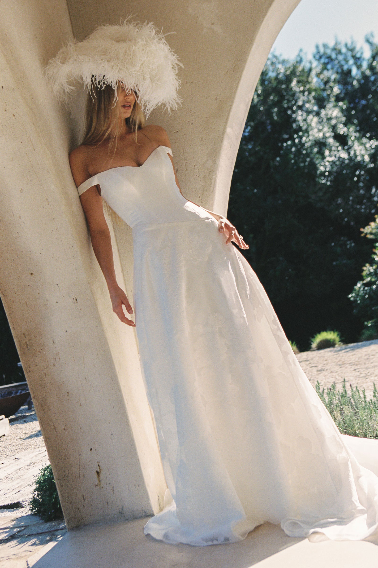 A woman wearing an off-the-shoulder white wedding dress with a fitted bodice and flowing skirt_XS_