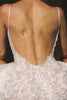 A close-up back view of a woman wearing a white lace bridal dress with an open back and layered delicate rose gold chain backlaces draped across her skin.
