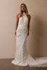 A woman modeling a sleeveless white wedding gown with floral lace applique and a long train against a plain beige studio wall_XS_