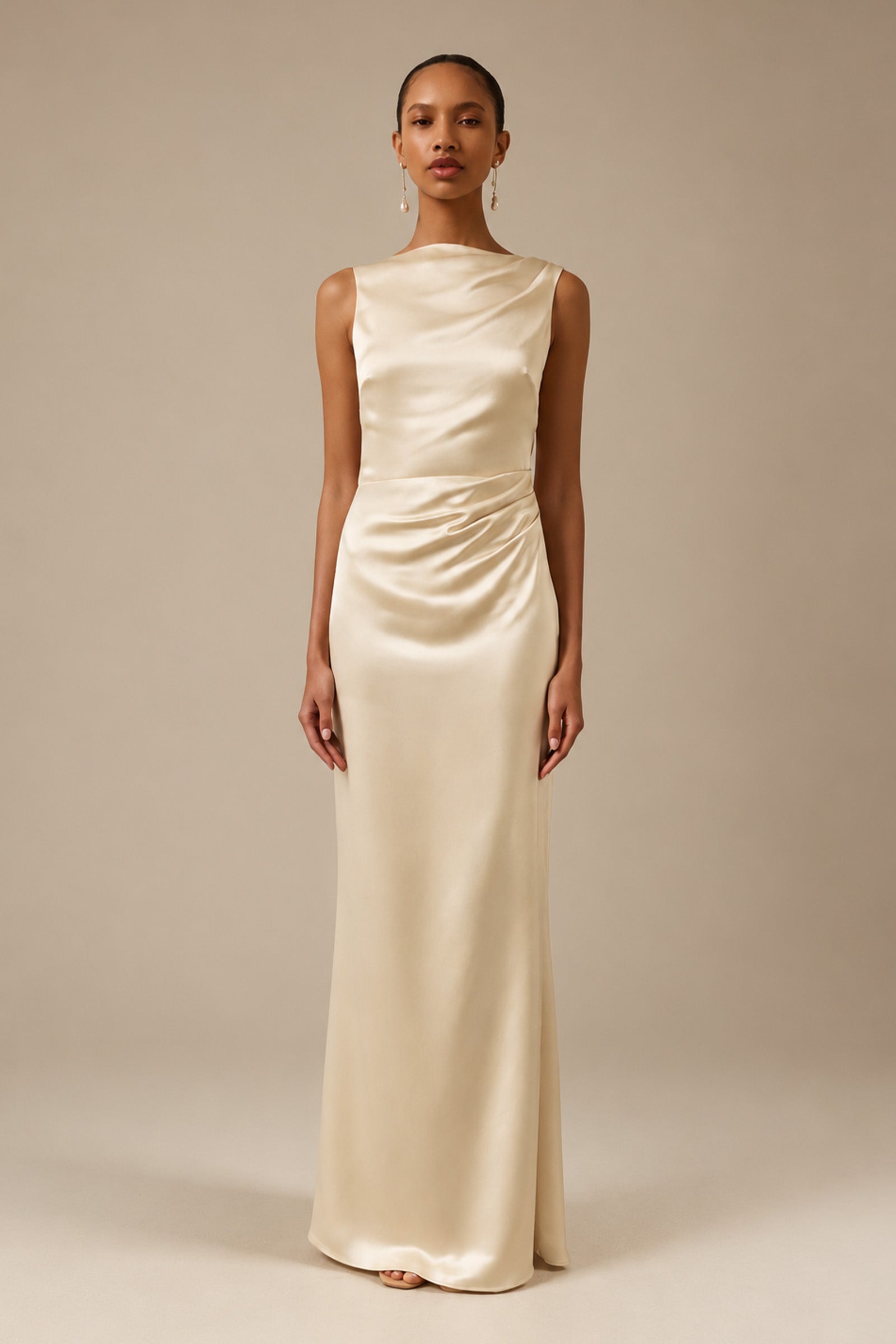 A woman modeling a sleeveless, floor-length cream satin gown with a draped, gathered bodice and skirt, set against a solid warm beige studio background_XS_
