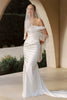 A woman wearing a white off-the-shoulder mermaid-style gown with long fringe draped over the arms and a matching veil, standing in a sunlit architectural setting with arches and greenery in the background.