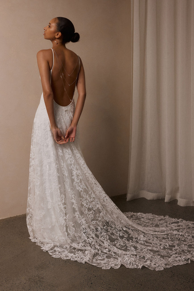 woman wearing a white lace backless dress with thin straps and delicate chain jewellery across her back