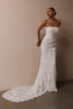 A woman wearing a strapless white lace wedding gown with a long train