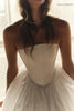 A close-up of a woman wearing a strapless ivory wedding dress with a structured corset-style bodice and a voluminous tulle skirt. 