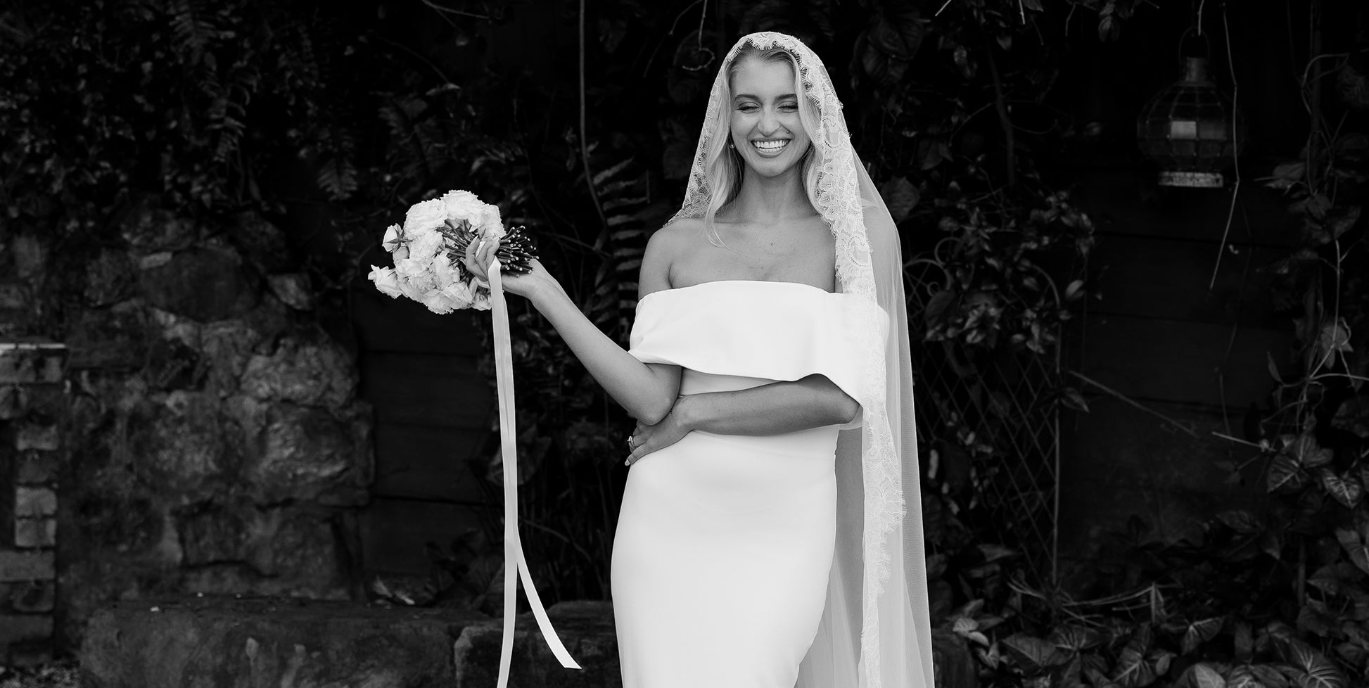 A bride in an off the shoulder wedding dress wearing a lace veil.
