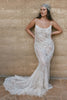 Woman wearing a lace wedding dress and headscarf against a stone wall.