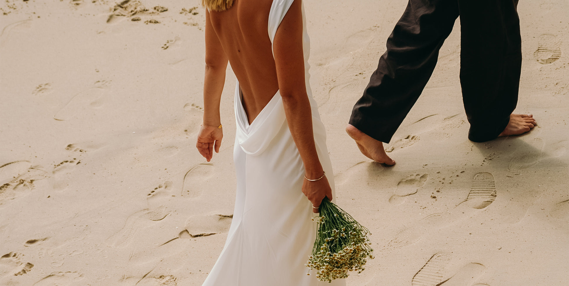 A bride and groom walking on a sandy beach.