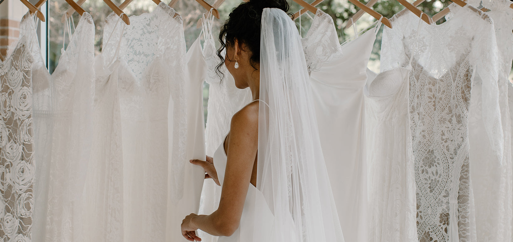 bride looking at wedding dresses hanging on rail